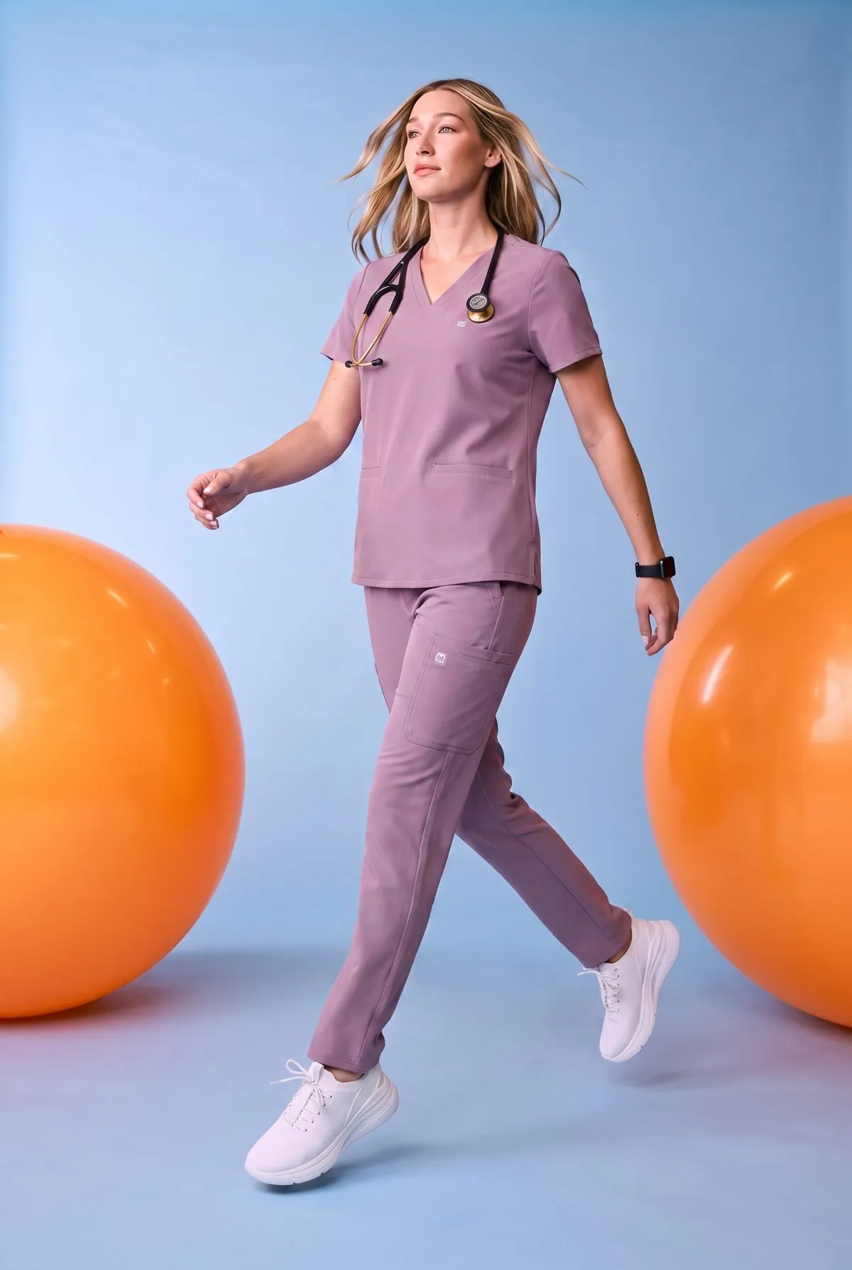 Model walking in mauve scrubs between exercise balls