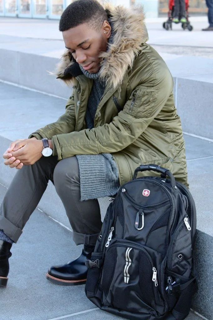 Man in a parka sitting with a SwissGear backpack