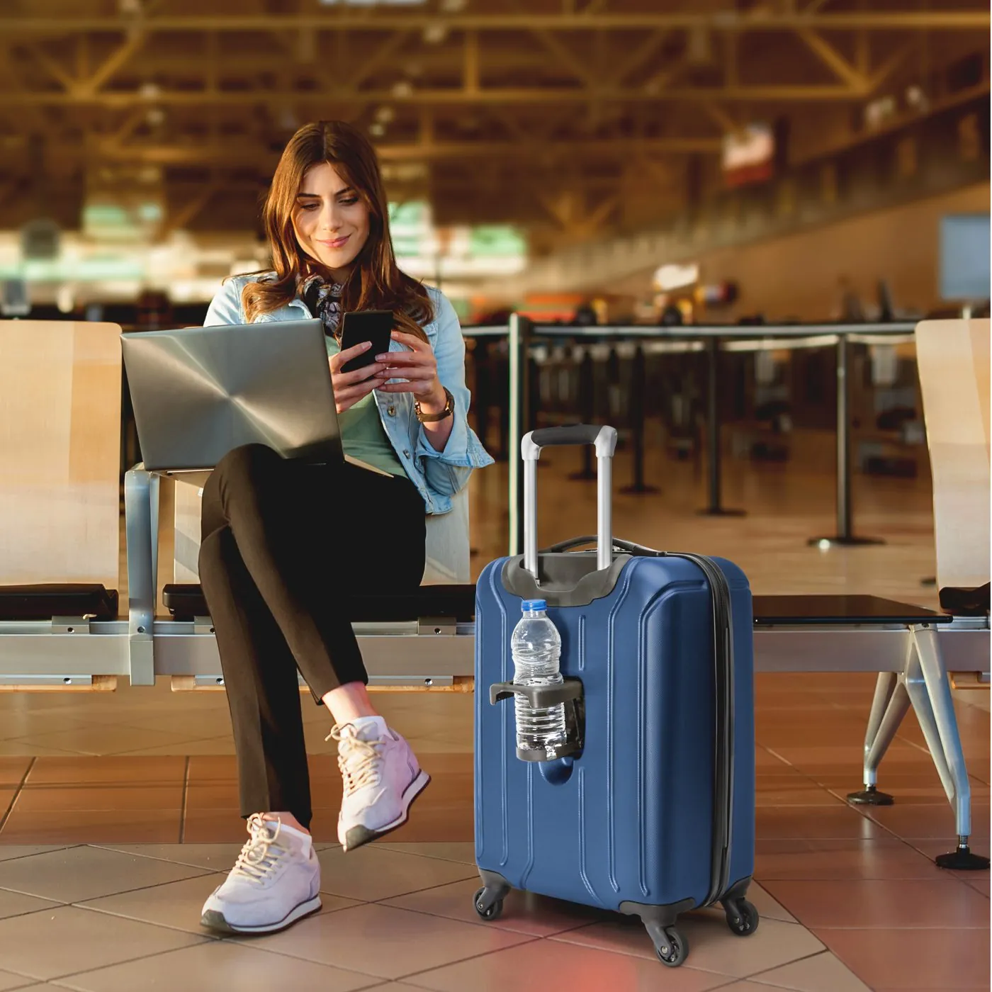 Woman on her laptop at an airport gate beside a blue SwissGear suitcase