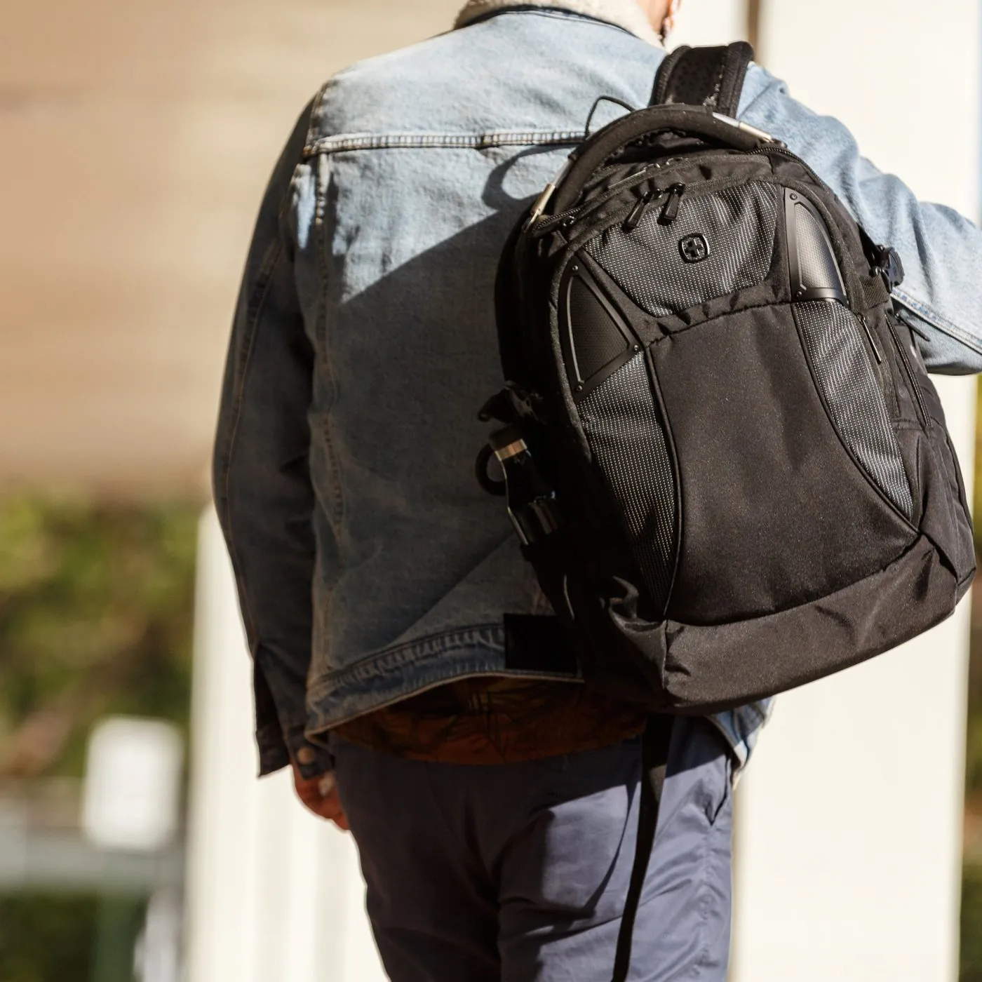 Man in a denim jacket carrying a SwissGear backpack