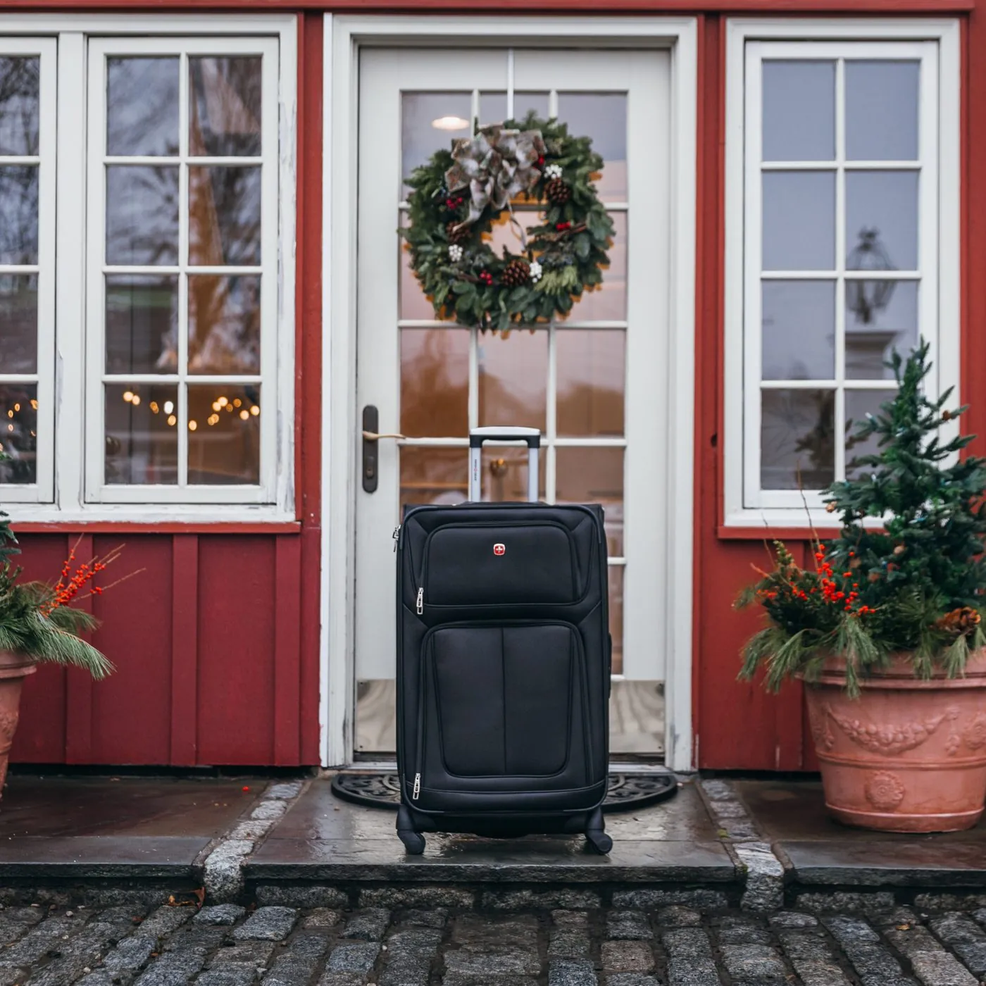 SwissGear suitcase at a red front door with a holiday wreath