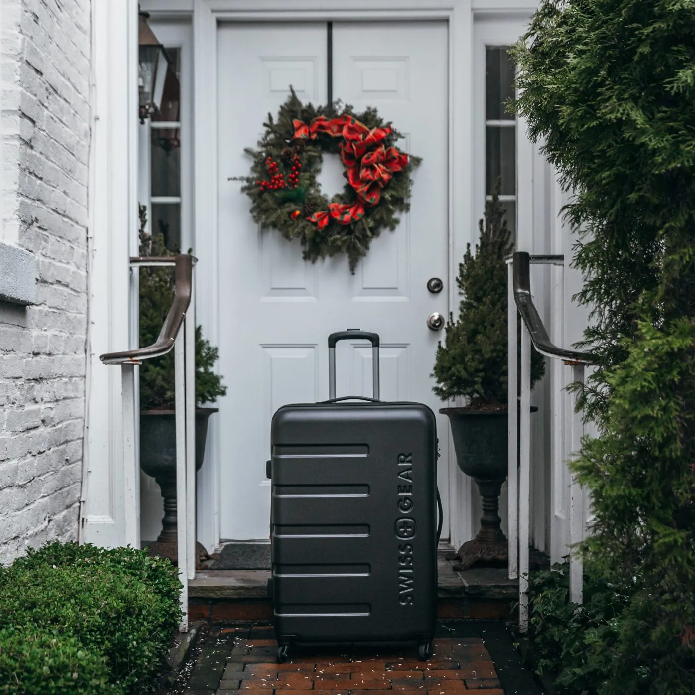 Black SwissGear suitcase at a white front door with a wreath