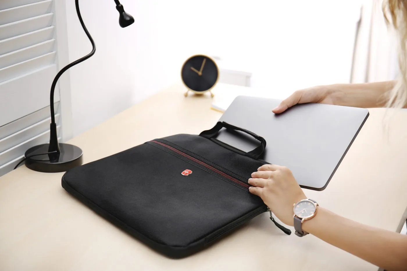 Laptop sliding into a SwissGear sleeve on a desk